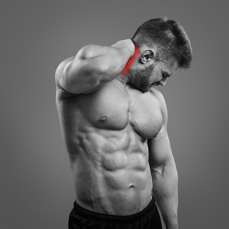 Muscular man suffering from neck pain. Front view over gray backgroundの写真素材
