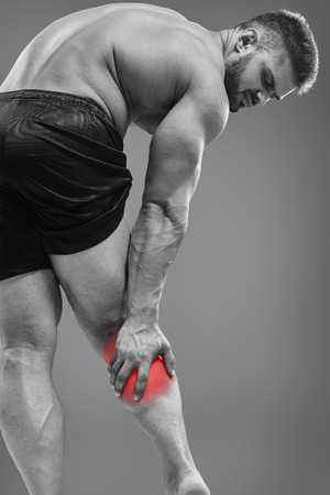 Muscle man having calf pain. Bodybuilder tension. Glowing red spot conceptの写真素材