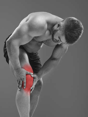 Sportsman holding hands on a sick knee, isolated on gray background. Glowing red spot conceptの写真素材