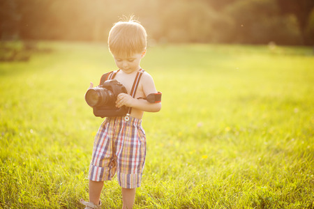 Beautiful smiling kid boy holding a DSLR camera in parkの写真素材