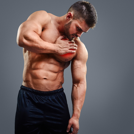 Muscular shirtless man with heart pain over gray background. Concept with highlighted glowing red spot.の写真素材