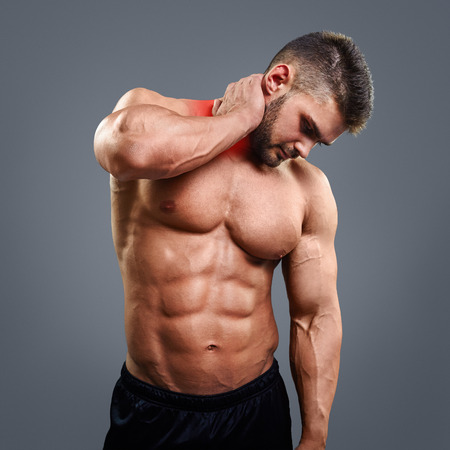 Muscular man suffering from neck pain. Front view over gray backgroundの写真素材