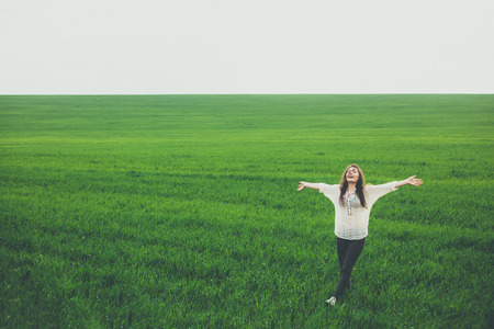 Happy young woman walking in green field. Pretty girl standing with arms raised in middle of meadow with copy space. Freedom, happiness, nature, summer concept.の写真素材