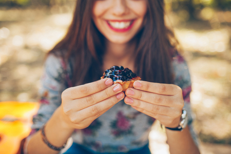 Closeup of smiling girl holding berries tartalet. Young woman hands close up with currant little cake and defocused backgroundの写真素材