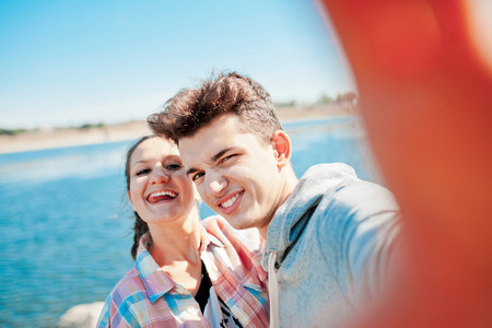 Young couple making a selfie outdoors and playing ape. Teenage girl and young man having fun with camera on a sunny dayの写真素材