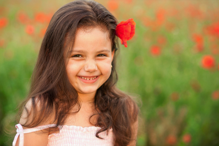 Adorable little girl in poppies. Beautiful smiling child outdoors in a fleld. Shy girl posing for camera in a meadow.の写真素材