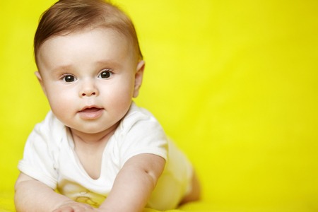 Surprised baby boy on his stomach looking to camera on yellow background. Cute infant kid over bright background.の写真素材