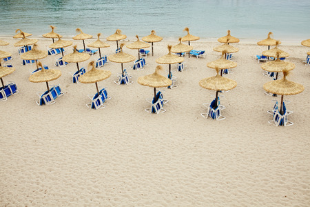 Group of umbrellas and sunloungers on empty beach. Nobody on beach. Rustic natural fiber umbrellas with copy space.の写真素材