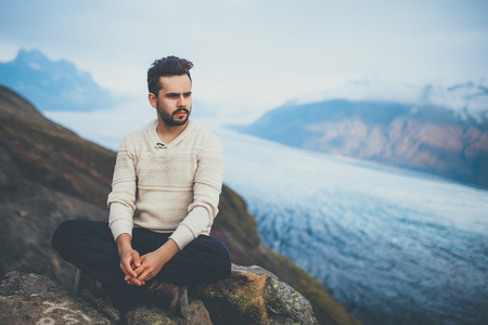 Handsome young man sitting outdoors near glacier Skaftafelljokull, Vatnajokull Iceland. Fashion male wearing warm sweater on a cold winter day in Iceland.の写真素材