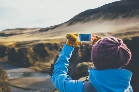 Back view of woman wearing winter clothes taking pictures of canyon in Iceland.の写真素材