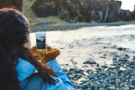 Rear view of woman taking picture of river with her smartphone in Iceland. Woman shooting Iceland...