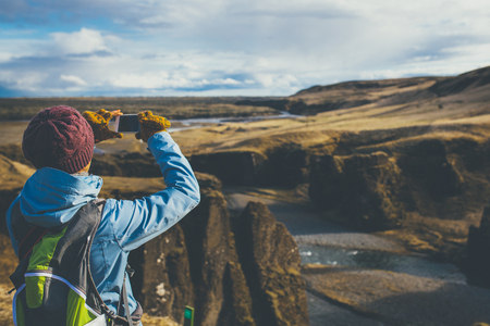 Back view of woman wearing winter clothes taking pictures of canyon in Iceland.の写真素材