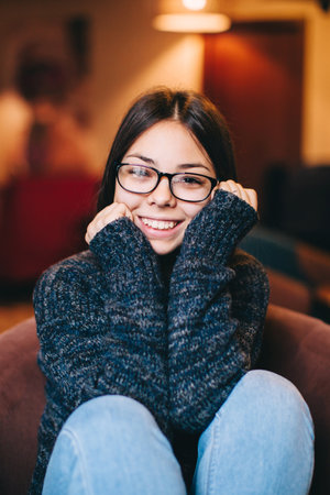 Shy teenage girl wearing eye wear sitting in cafe,smiling, relaxing.の写真素材