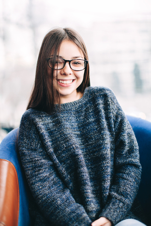portrait of pretty young woman wearing eyeglasses, sitting in a cafe and smilingの写真素材