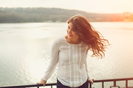 Young plus size woman staying outdoors near a lake on sunsetの写真素材