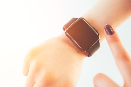 Woman using smart watch touching empty screen with a finger. Closeup of hands and wrist with smartwatch display isolated over white background with sunflareの写真素材
