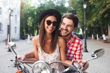 Young pretty fashion vintage hipster couple having fun outdoor on scooter in summer. Girl in hat and sunglasses riding a scooter with her boyfriend.の写真素材