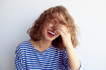 Laughing woman in marine shirt with curly hair over white wall. Toothy smile and red lips.の写真素材