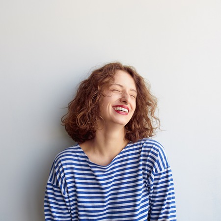 Square portrait of hipster woman laughing with eyes closed on white background. Curly cute girl smilingの写真素材