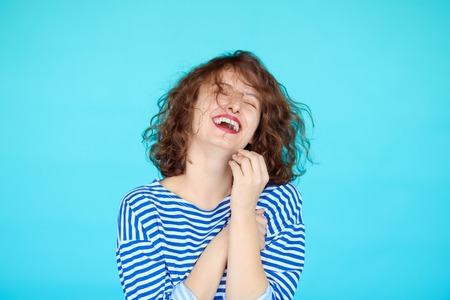portrait of laughing hipster teenage girl against blue color background. Happy young woman in striped clothes in marine style isolatedの写真素材