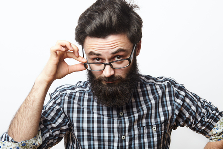 Confident young bearded man in eyeglasses looking at camera. Suspicious male teacher with beard staring isolated on white backgroundの写真素材