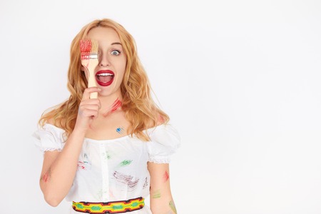Surprised Woman Holding a Paint Brush. Cheerful young girl artist tries different colors over white backgroundの写真素材