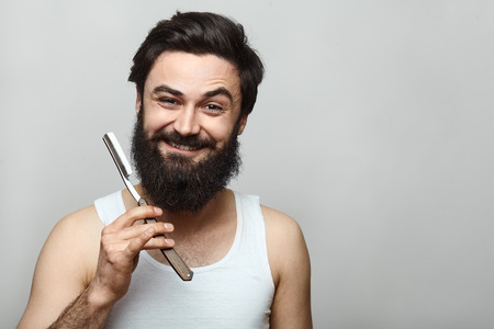 young man shaving in the bath. He is passing the razor for the beard while it looks at the camera