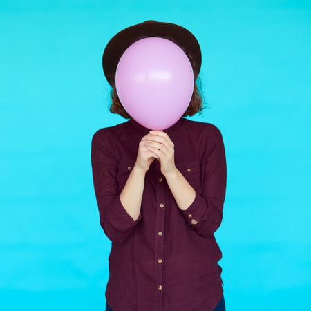 Young hipster woman holding balloon over her face. Pink and turquoise colors fashion conceptの写真素材