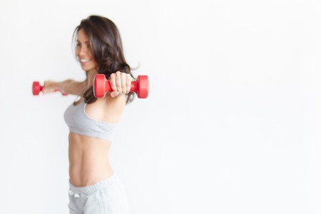 Hand with dumbbell in focus. Beautiful young woman holding dumbbells isolated on white background with blank space. Abstract concept of workout and fitnessの写真素材