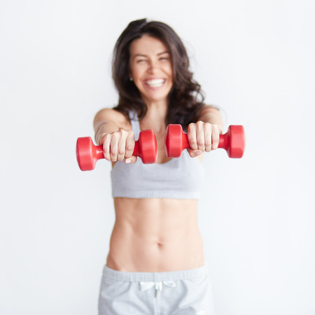 Selective focus on hands. Defocused happy fitness woman lifting dumbbells smiling cheerful isolated on white backgroundの写真素材