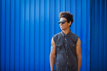 Cool young afro american curly young man in front of blue wall background and copy space