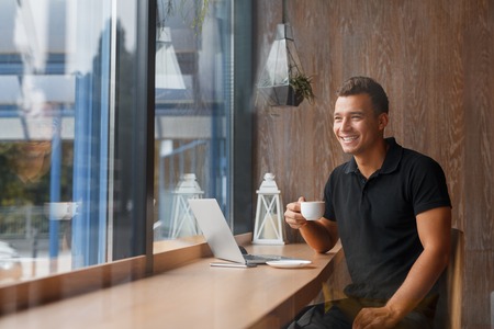 businessman drinking coffee in the city cafe during lunch time. Young man in black tshirt smiling indoors with copy spaceの写真素材