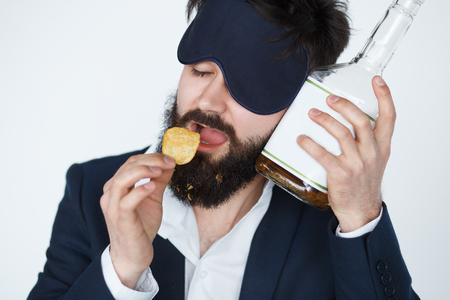 Drunk man feeling bad after drinking, eating crisps, alcoholism concept on white backgroundの写真素材