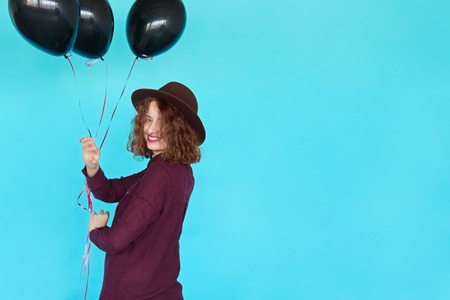 Trendy young happy woman with black balloons having a birthday party. Fashion hipster girl wearing stylish clothes on blue background and copy spaceの写真素材