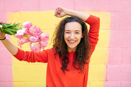 beautiful girl in red sweater on colorful yellow and pink background. Smiling happy young woman holding a flowers bouquetの写真素材