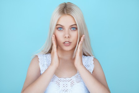 Wide eyed young teenage girl in shock over blue background. Fashion model with white hair surprised isolated on color backgroundの写真素材