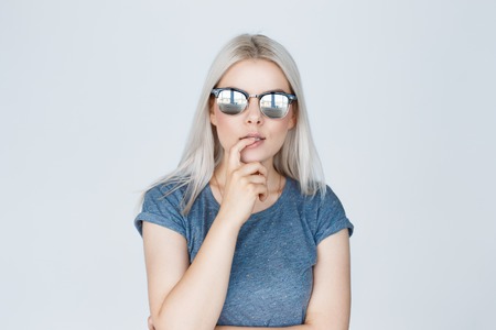 Seductive blonde girl wearing mirror sunglasses isolated on a gray background. Closeup portraitの写真素材