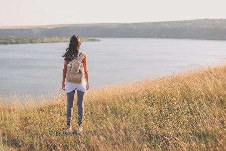 Back view of hipster young girl with backpack enjoying view on cliff. Tourist traveler on background view. Full body Mockup with copy space. filter effectの写真素材