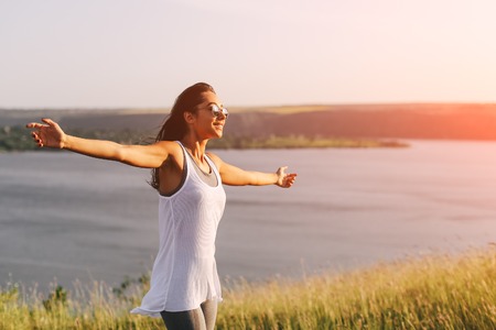 Successful sporty woman raising arms towards golden beautiful sunset and sea. Girl on cliff with copy space and lens flareの写真素材