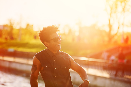 Curly stylish handsome african american young man smiling at sunset with sunlight effect.の写真素材