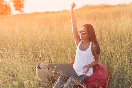 Euphoric woman searching job with a laptop in a meadow. Working at computer outdoors in nature. Happy girl with 4g internet connectionの写真素材