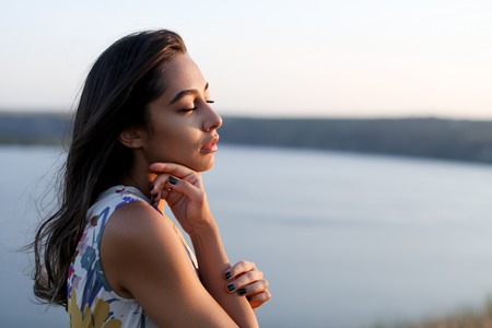 beautiful girl enjoying wind and breathing Spanish young woman in summer dress touching skin faceの写真素材
