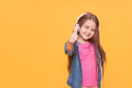 cute little girl showing thumbs up isolated one yellow backgroundの写真素材