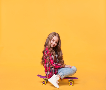happy child girl sitting on skateboard over yellow color background with copy space above headの写真素材