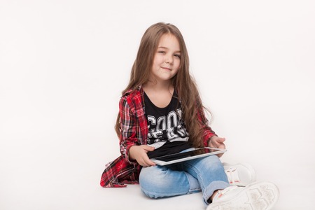education and technology concept - little student girl sitting, holding a tablet and doing homework over white backgroundの写真素材