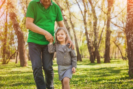 Lovely girl walking with grandfather in parkの写真素材