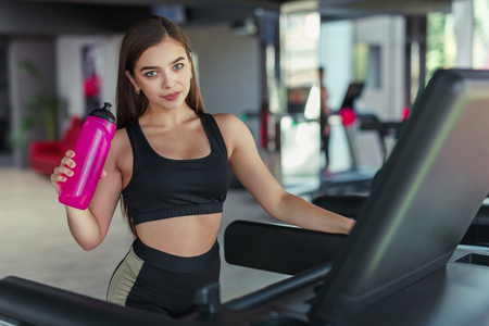 Young sportswoman posing with bottle on treadmillの写真素材