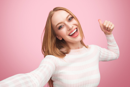 Cheerful woman taking selfie and gesturing thumb-upの写真素材