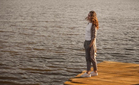 Casual pensive woman on pier above lakeの写真素材