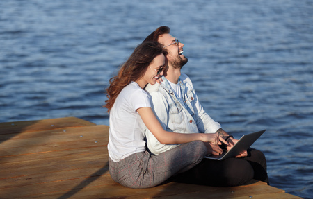 Happy couple with laptop chilling on pierの写真素材